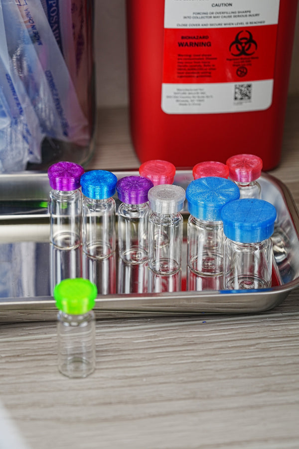 Watch out for fake bacteriostatic water — peptide vials lined up in an inspection tray next to a red biohazard sharps container for safety verification