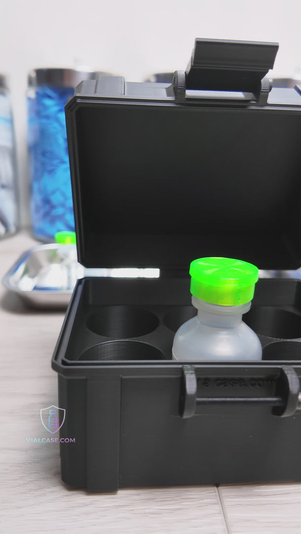 Empty vial case opened to display six individual slots designed for bacteriostatic water vials. The interior is clean and structured for secure storage. The case sits on a tabletop with medical supplies and trays visible in the background.